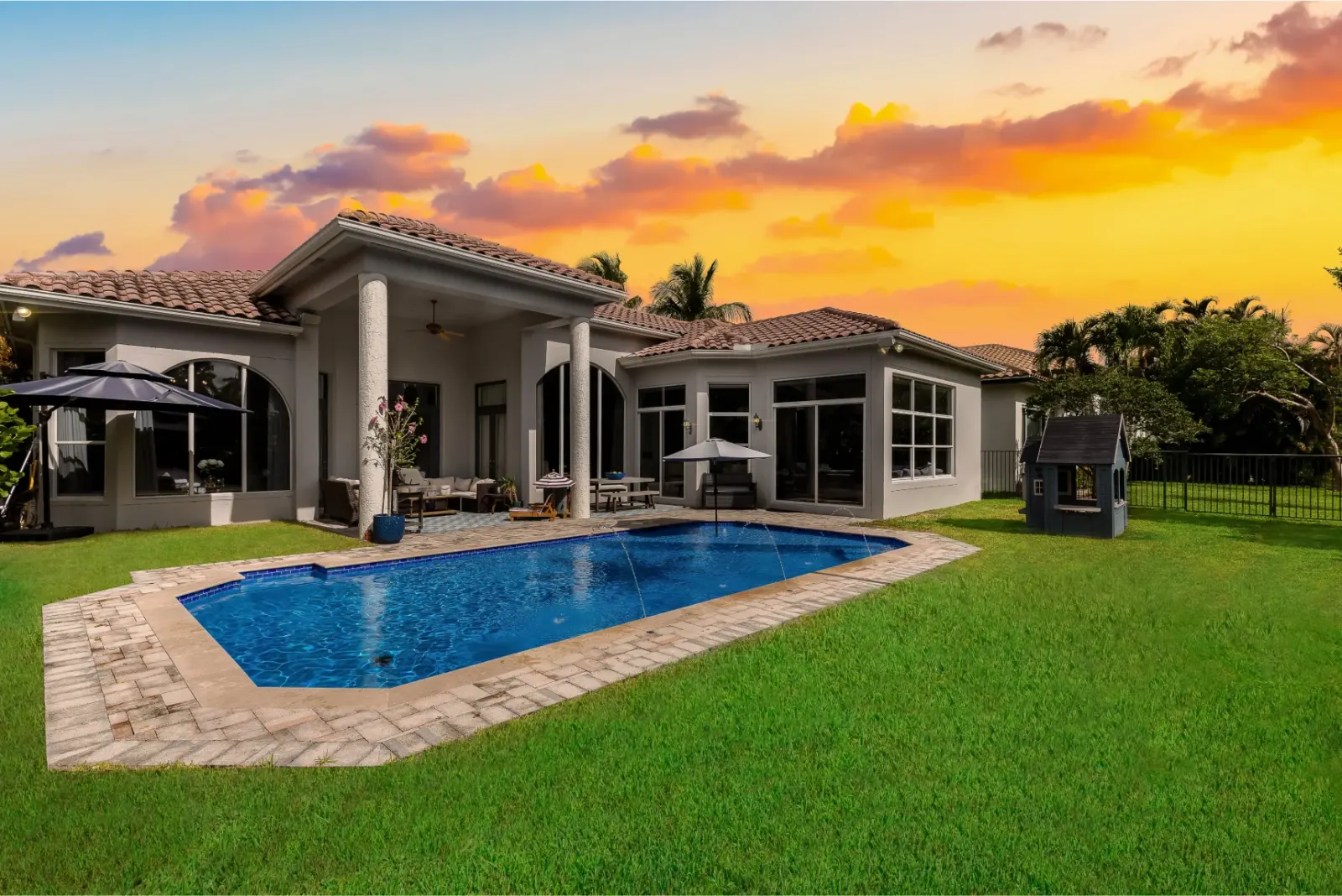 Luxury home with a backyard pool and covered patio at sunset.