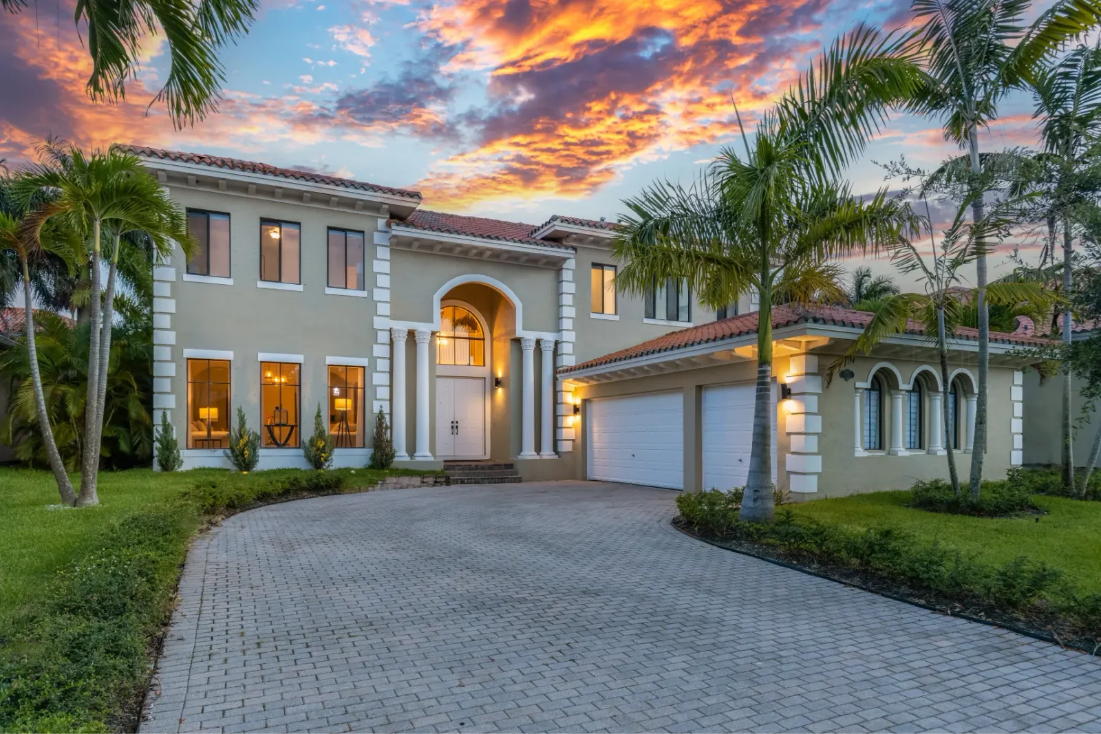 Grand two-story home with white columns and palm trees at sunset.