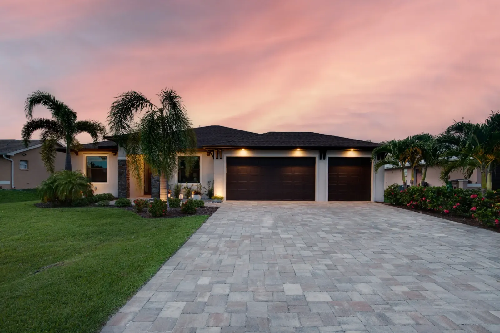 Contemporary single-story home with a three-car garage and palm trees at sunset.
