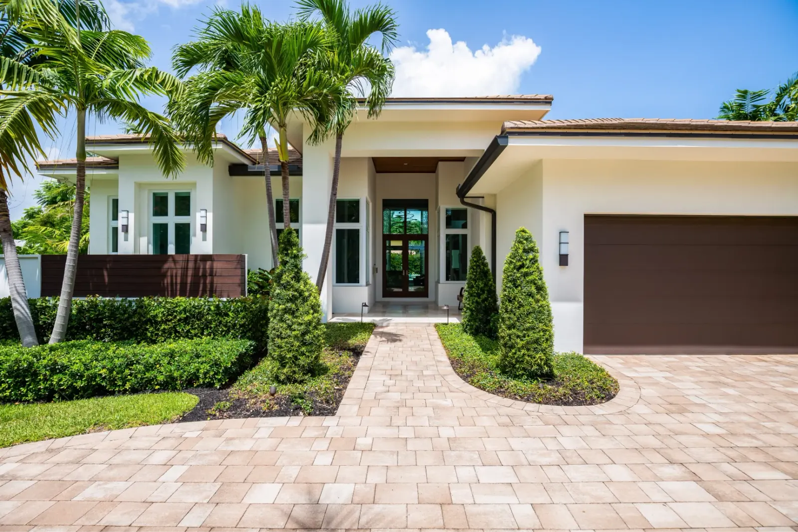 Elegant home with palm trees and a paved driveway.