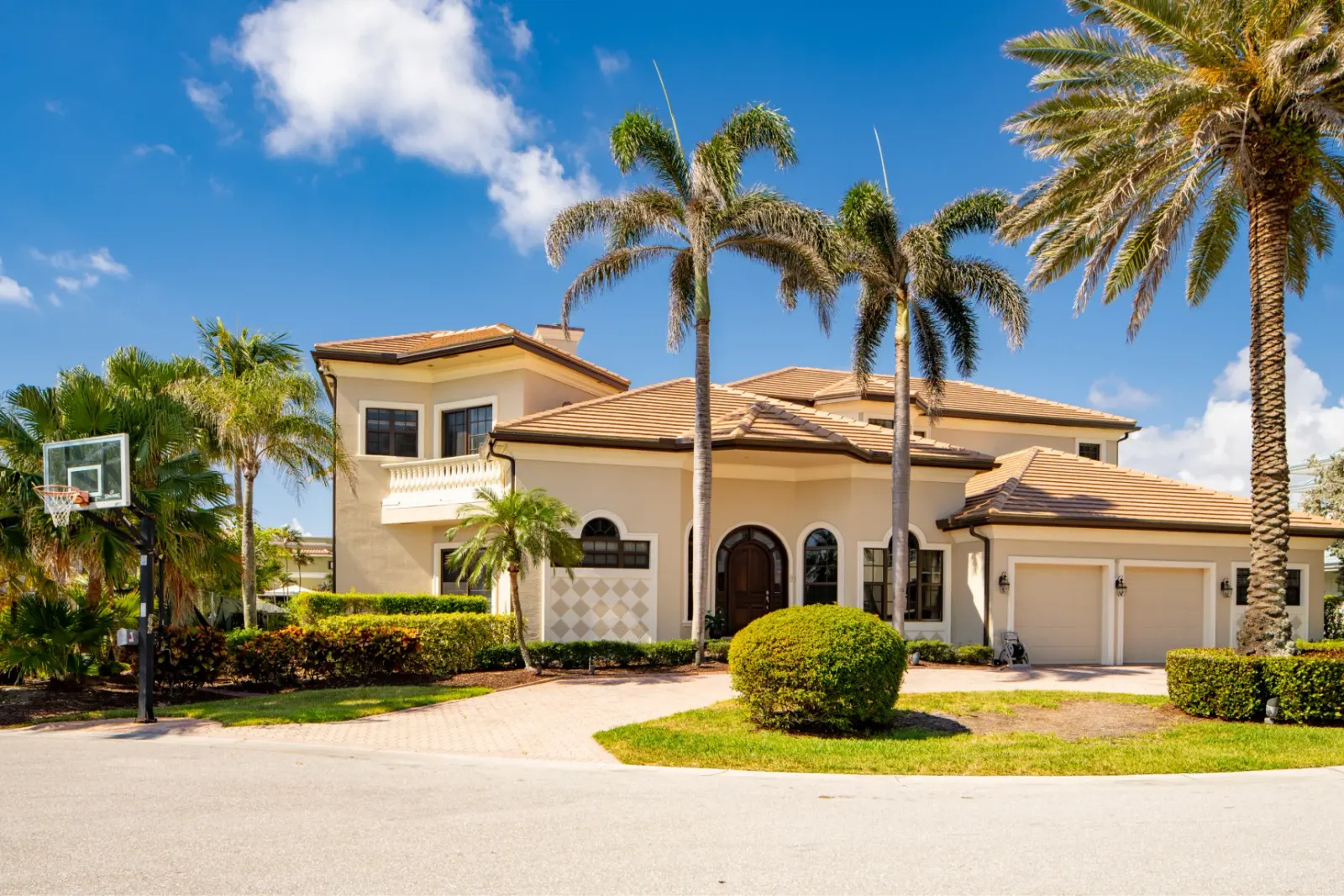 Elegant two-story home with palm trees and a basketball hoop.